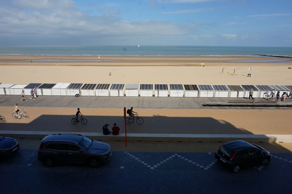 Het brede strand van Oostende met witte strandcabines en fietsers op de Zeedijk